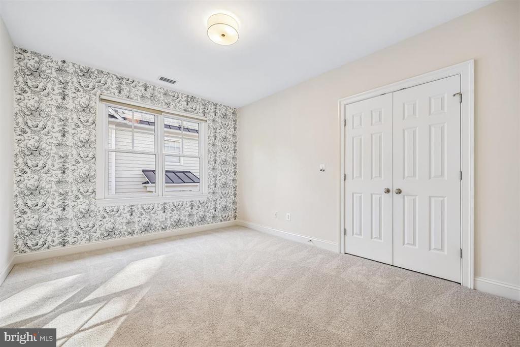 Empty bedroom with patterned wallpaper, beige carpet, a window, and white double closet doors.
