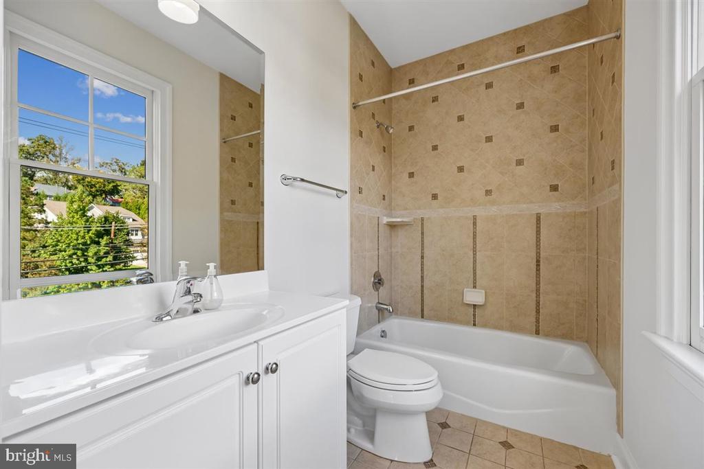 Bathroom with a white vanity, toilet, and tub with tan tile surround beside a window.
