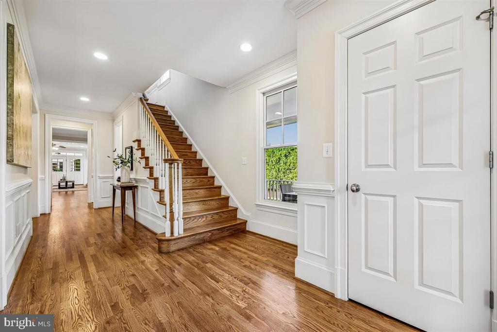 Entry foyer with hardwood floors, a wooden staircase, white paneled walls, and a window overlooking greenery.