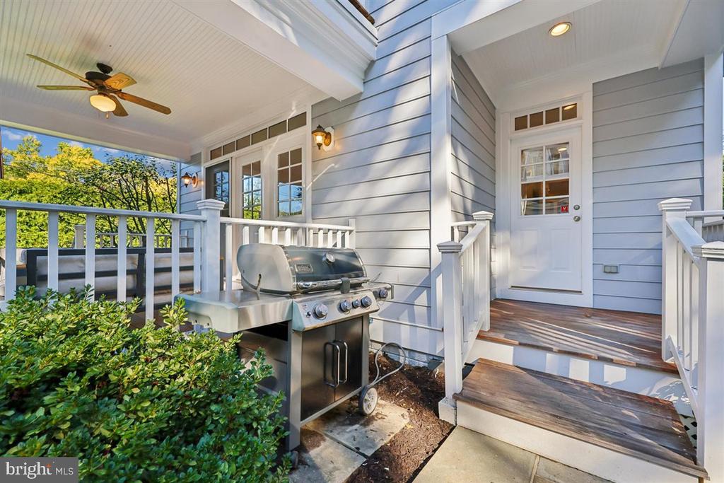 Covered porch with a stainless-steel grill beside the white-railed steps and front door.