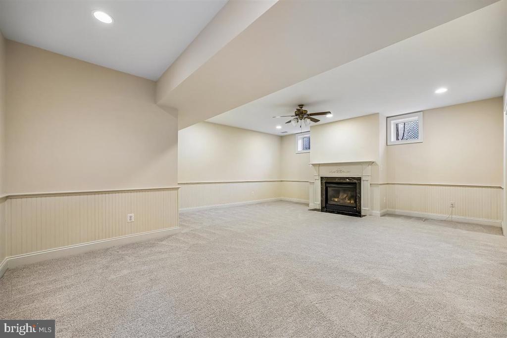 Vacant carpeted family room with a fireplace, wainscoting, and ceiling fan.