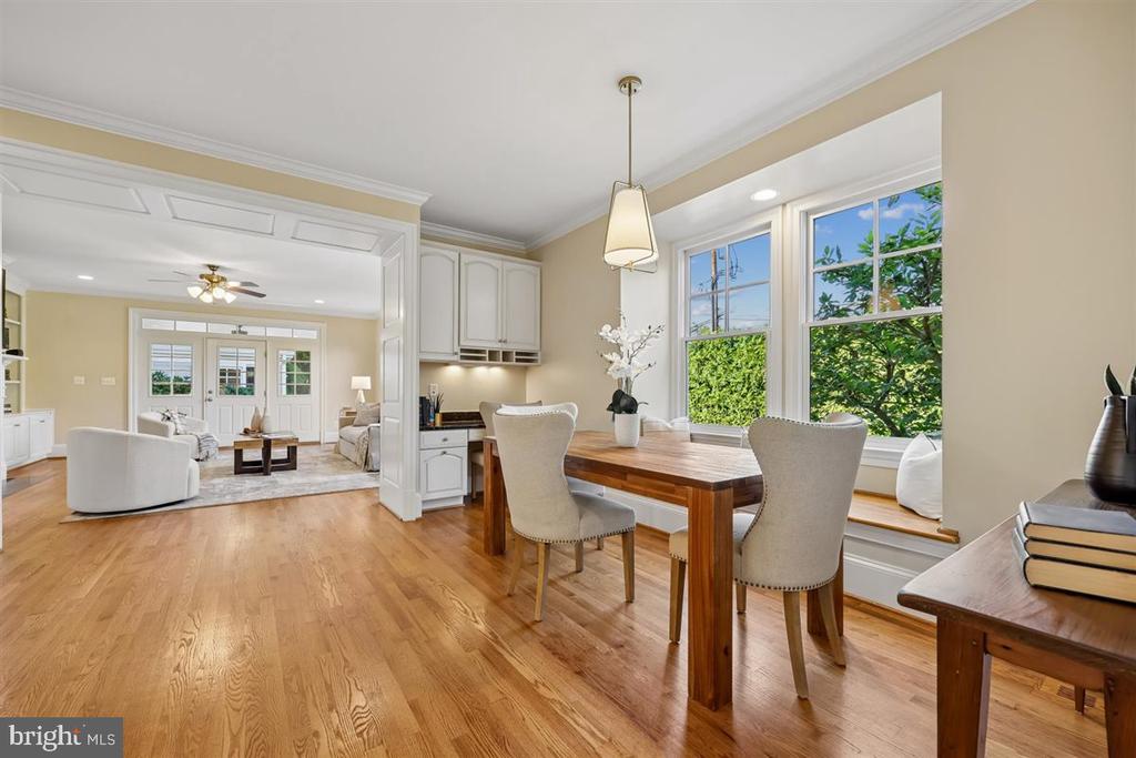 Dining area with a wooden table beside large windows, open to a living room with French doors.