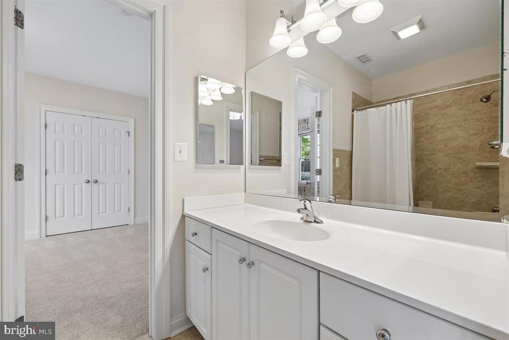 Bathroom with a long white vanity, mirrored wall, and tiled shower behind a white curtain.