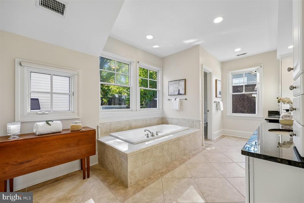 Bathroom with a tiled soaking tub beneath large windows and a dark countertop vanity.