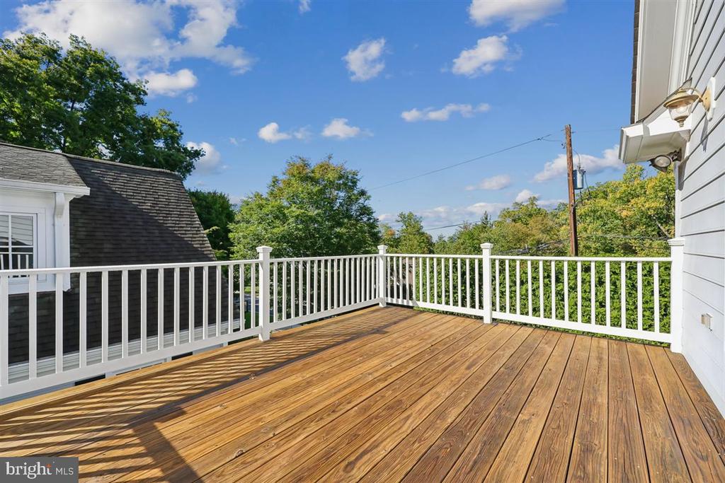 Wood deck with white railings overlooking leafy trees and neighboring rooftops.