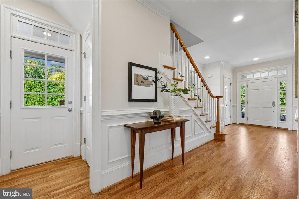 Entry foyer with hardwood floors, white wall paneling, and a staircase with a wood handrail.