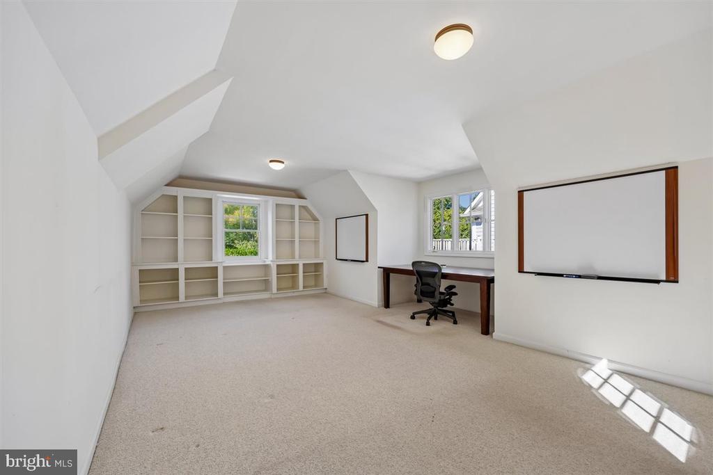 Home office with built-in shelves, a desk, and sloped ceiling.