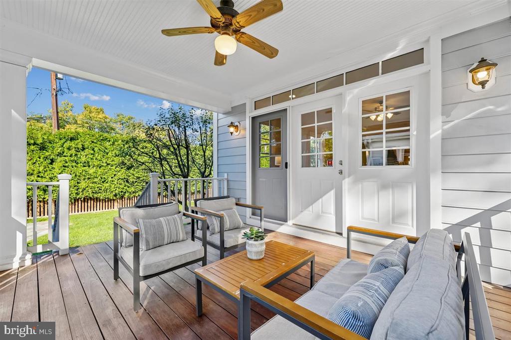 Covered porch with gray seating, a wooden coffee table, and views of the green yard.