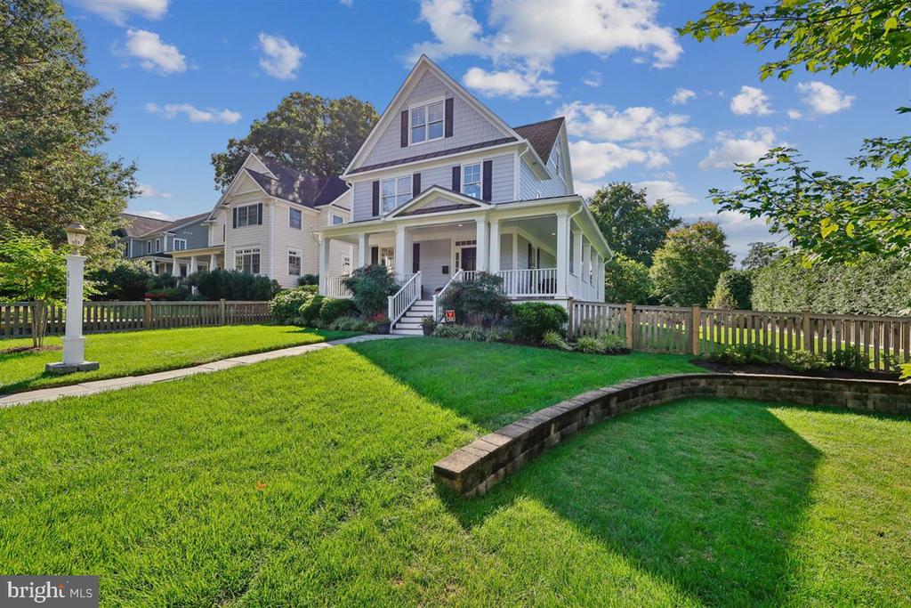 Two-story house with a covered porch, broad green lawn, and picket fence.