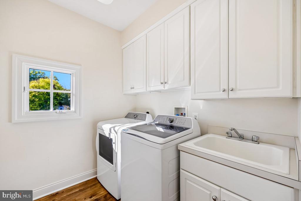 Laundry room with washer and dryer, white cabinets, utility sink, and a window overlooking trees.
