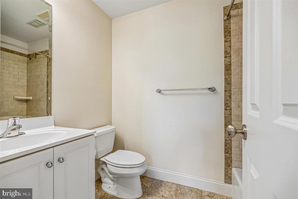 Bathroom with a white vanity and toilet, mirrored wall, and beige tiled shower.