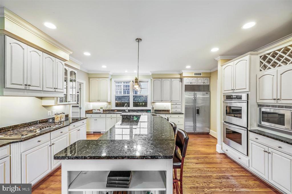 Kitchen with a large granite island, white cabinets, stainless steel appliances, and hardwood floors.
