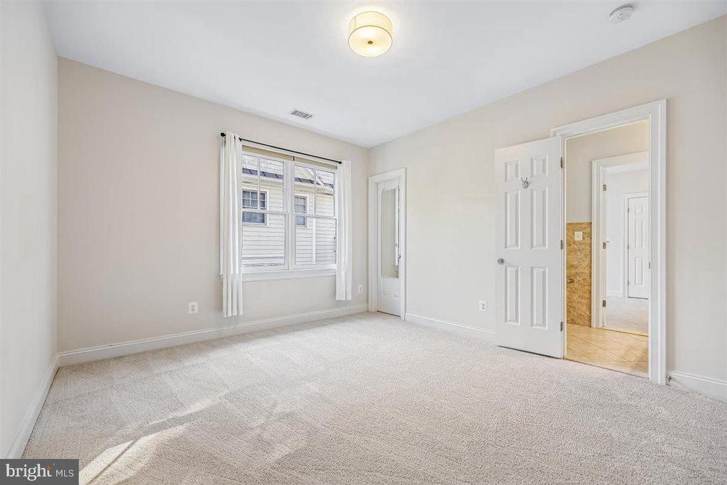 Empty carpeted bedroom with a curtained window and an open doorway to a tiled bathroom.