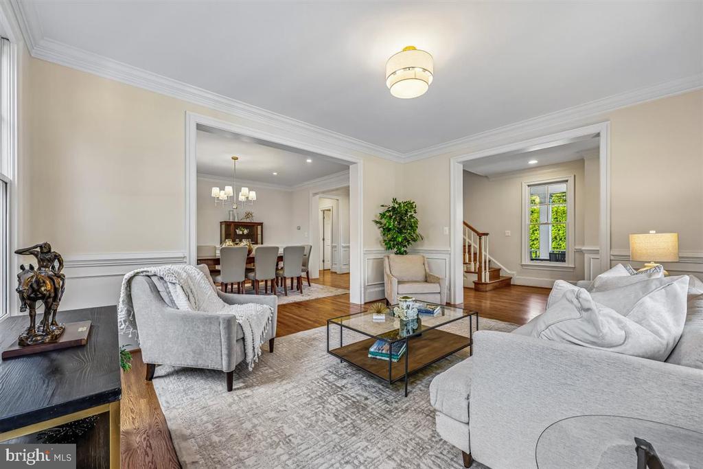 Living room with white seating, a glass coffee table, hardwood floors, and open views into adjoining rooms.