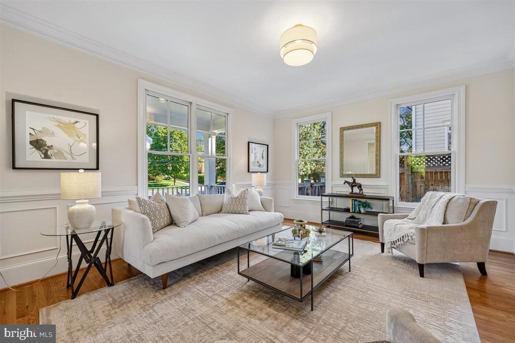 Staged living room with a white sofa, glass coffee table, and tall windows overlooking greenery.