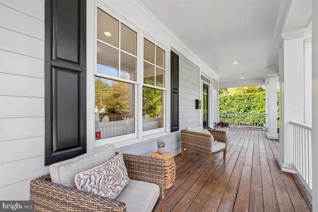 Covered porch with wicker seating, white siding, black shutters, and a wood plank floor.