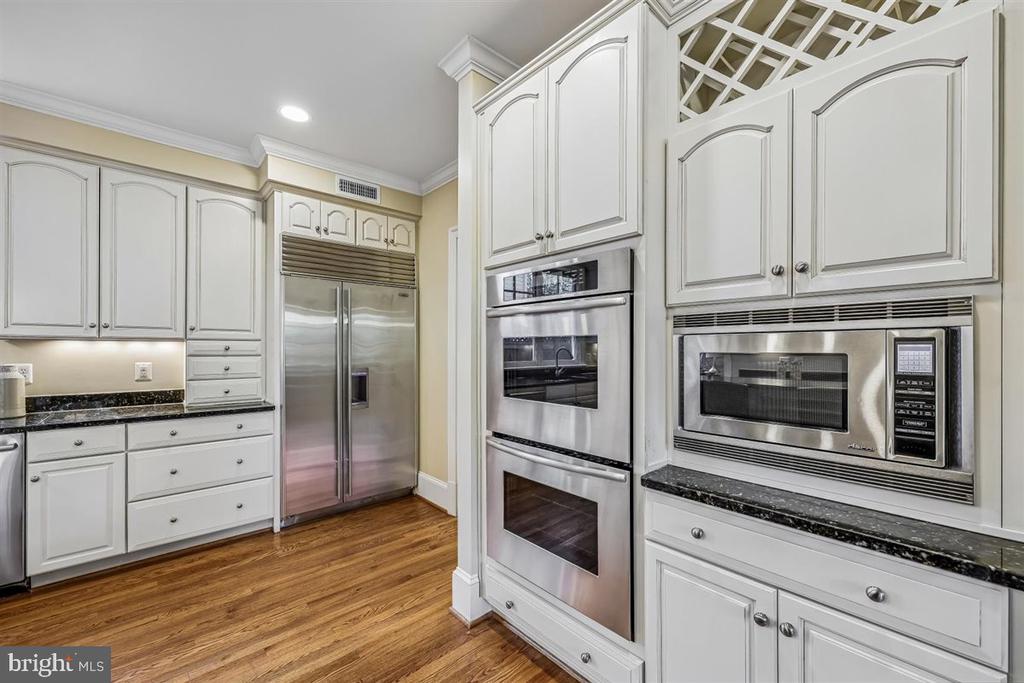 Kitchen with white cabinetry, stainless steel appliances, dark countertops, and hardwood floors.