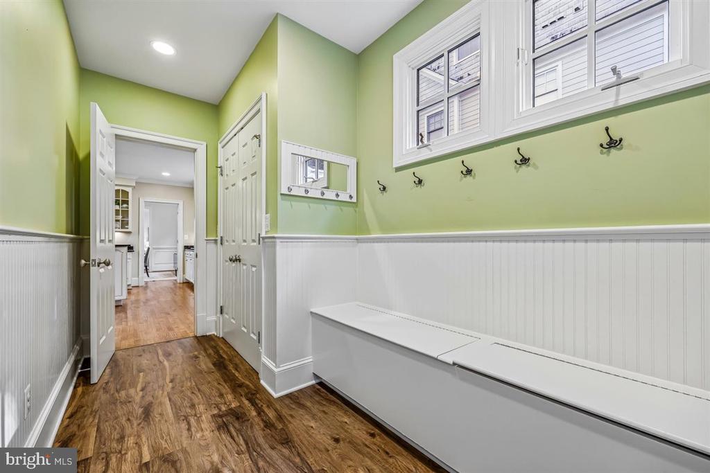 Mudroom with a built-in bench, coat hooks, pale green walls, and hardwood flooring.