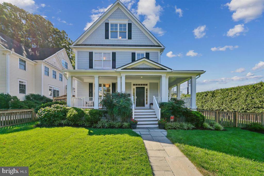 Two-story gray house with a covered porch, dark shutters, and a walkway across the lawn.