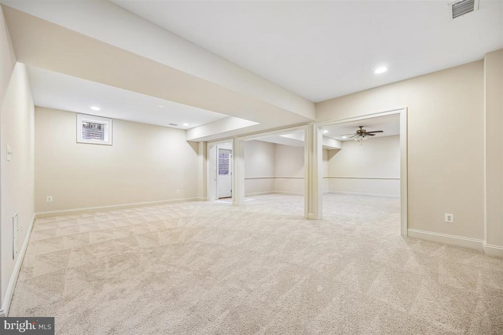 Finished basement with beige carpet and open adjoining rooms separated by support columns.