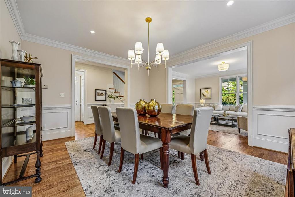 Dining room with a dark wood table, upholstered chairs, chandelier, and open connection to the living room.