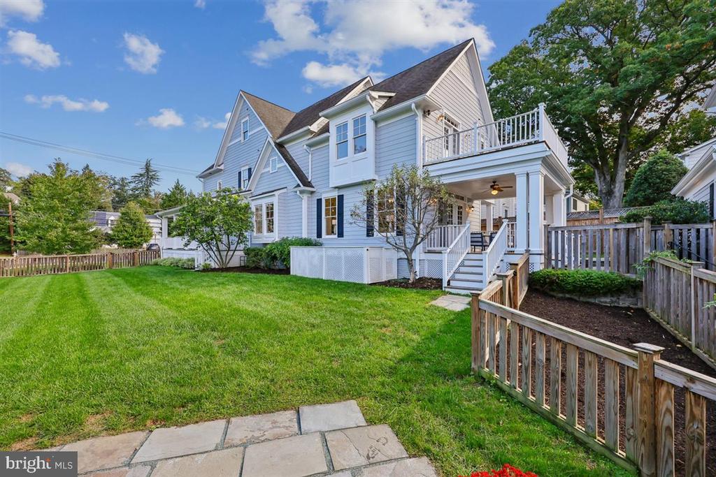 Light-blue multi-story house with a covered deck, fenced lawn, and patio.