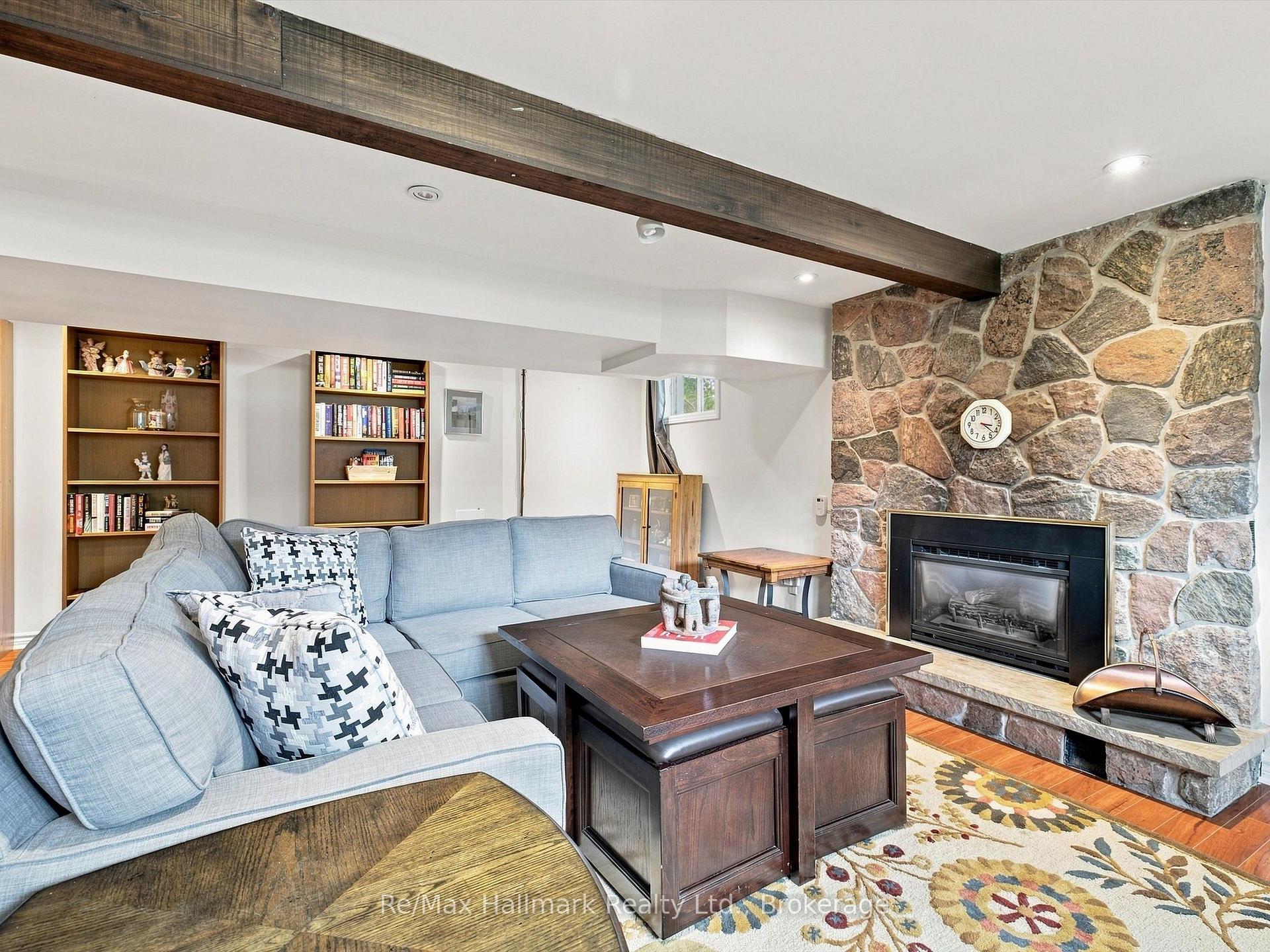 Living room with a stone fireplace, pale blue sectional, built-in bookshelves, and exposed wood beam.