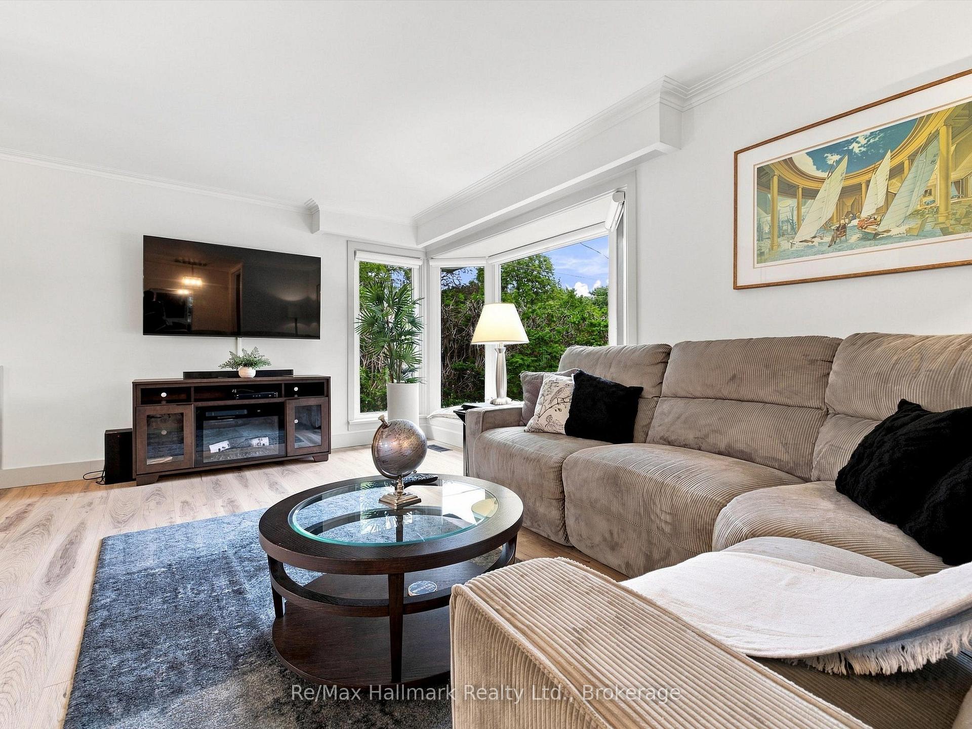 Living room with a beige sectional, round glass coffee table, and bright corner windows overlooking trees.