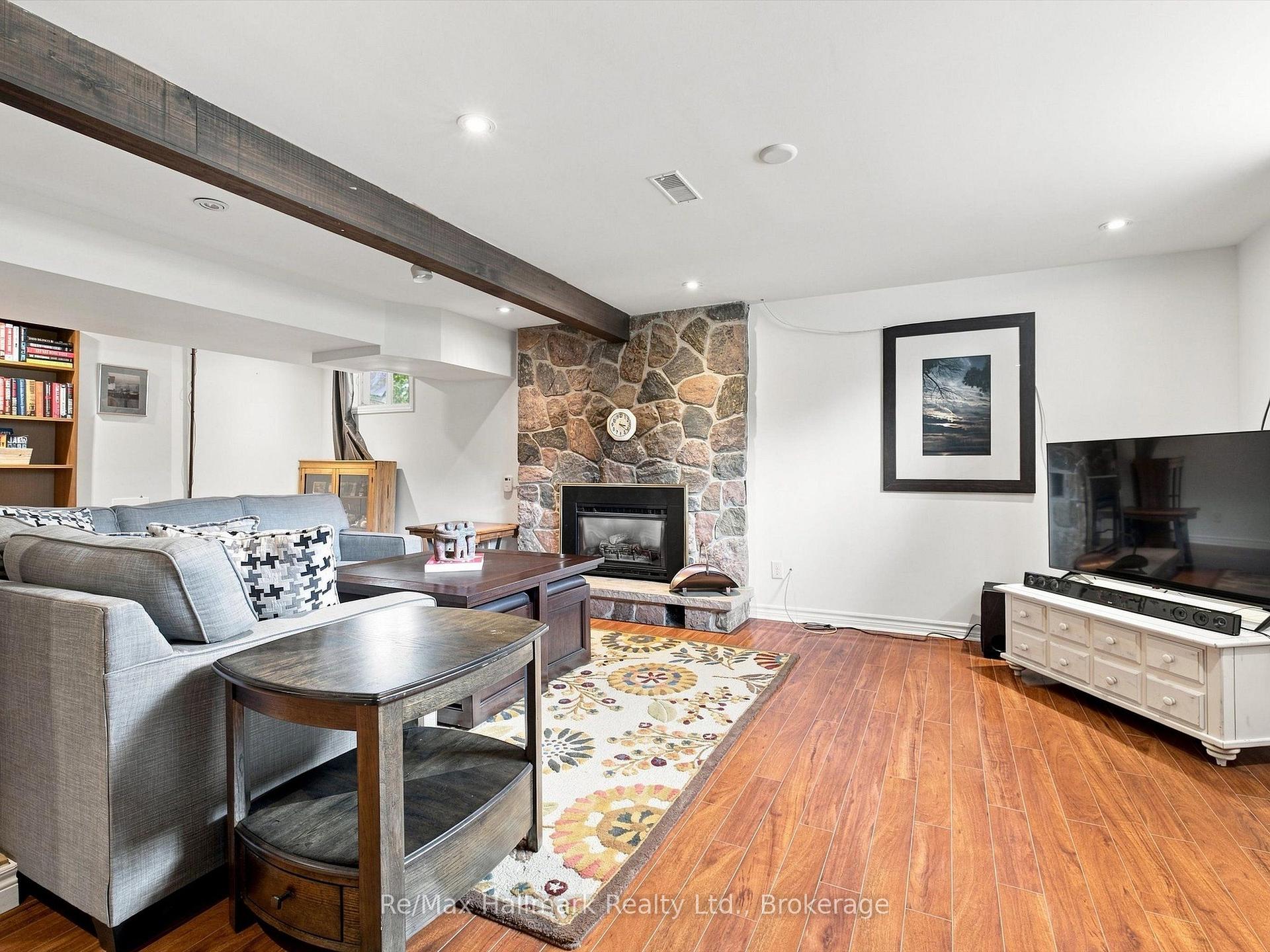 Living room with a stone fireplace, gray sectional, patterned rug, and wood-look flooring.