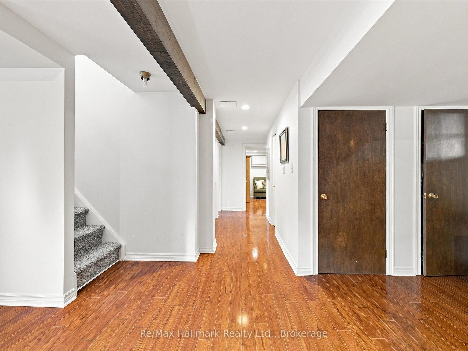 Hallway with hardwood floors, exposed ceiling beams, dark doors, and carpeted stairs.