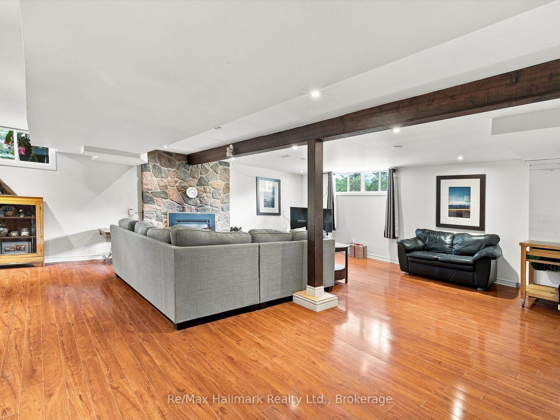 Living room with a stone fireplace, gray sectional, black leather sofa, and warm wood floors.