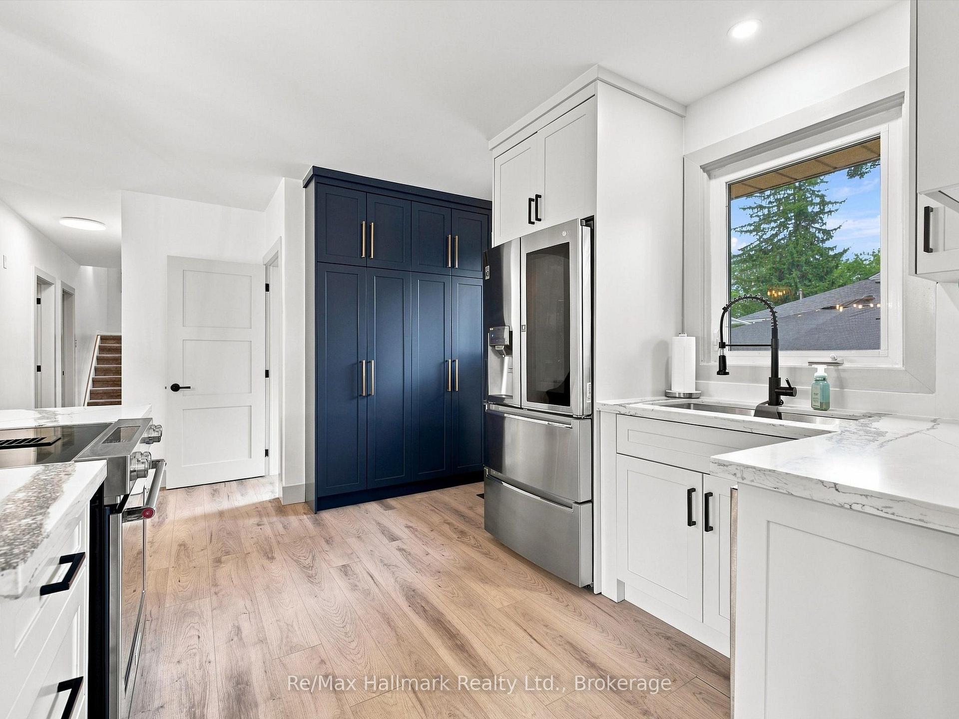 Renovated kitchen with navy cabinetry, stainless steel appliances, and a farmhouse sink beneath a window.