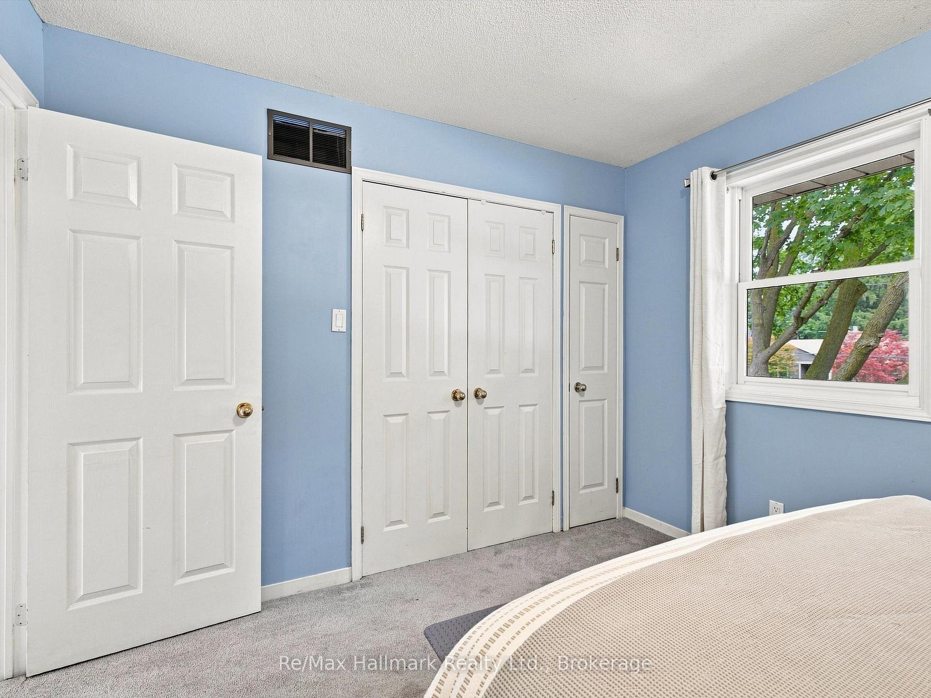 Bedroom with blue walls, white closet doors, gray carpet, and a window overlooking trees.