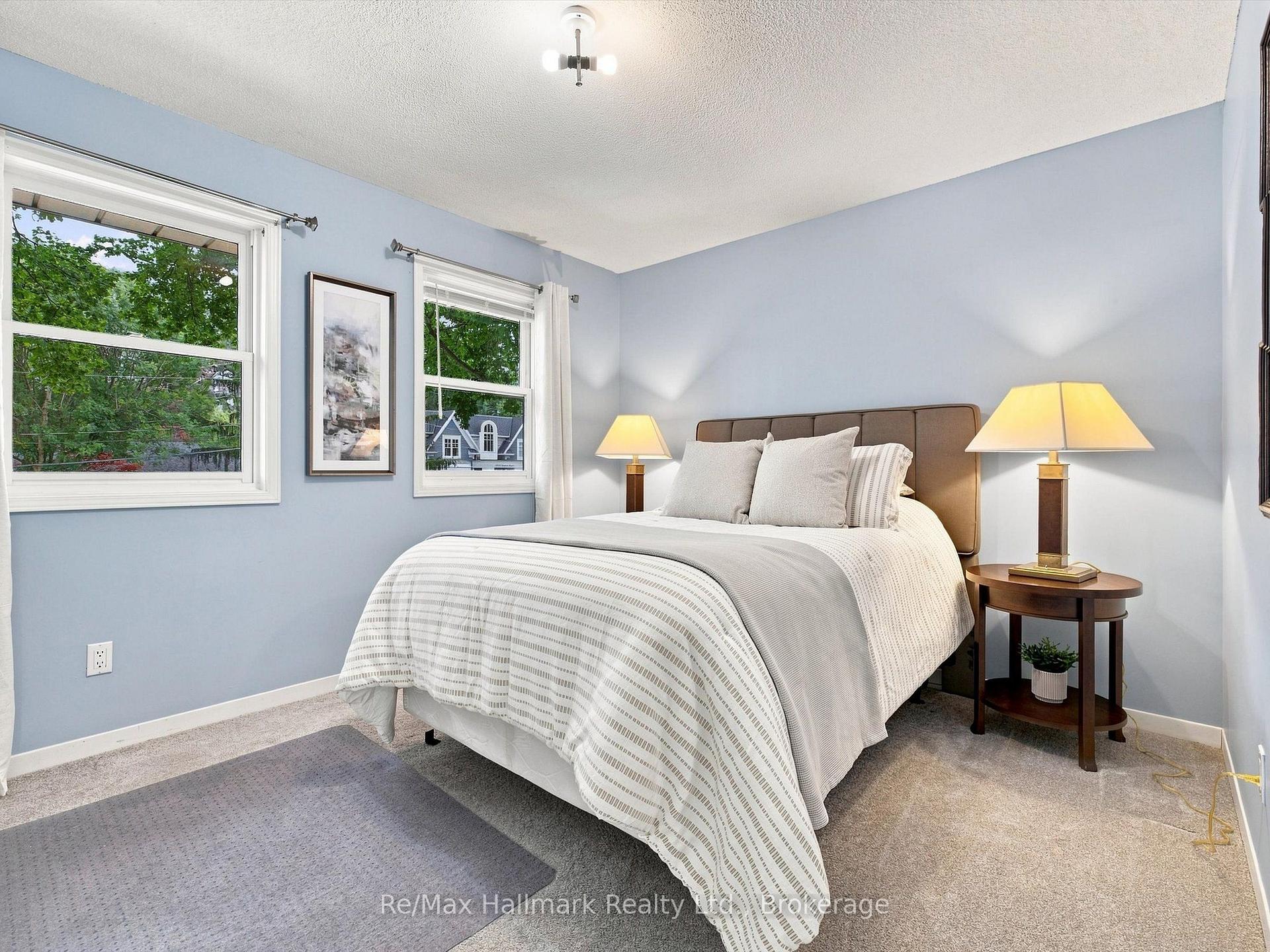Bedroom with a large bed, pale blue walls, and two windows overlooking leafy trees.
