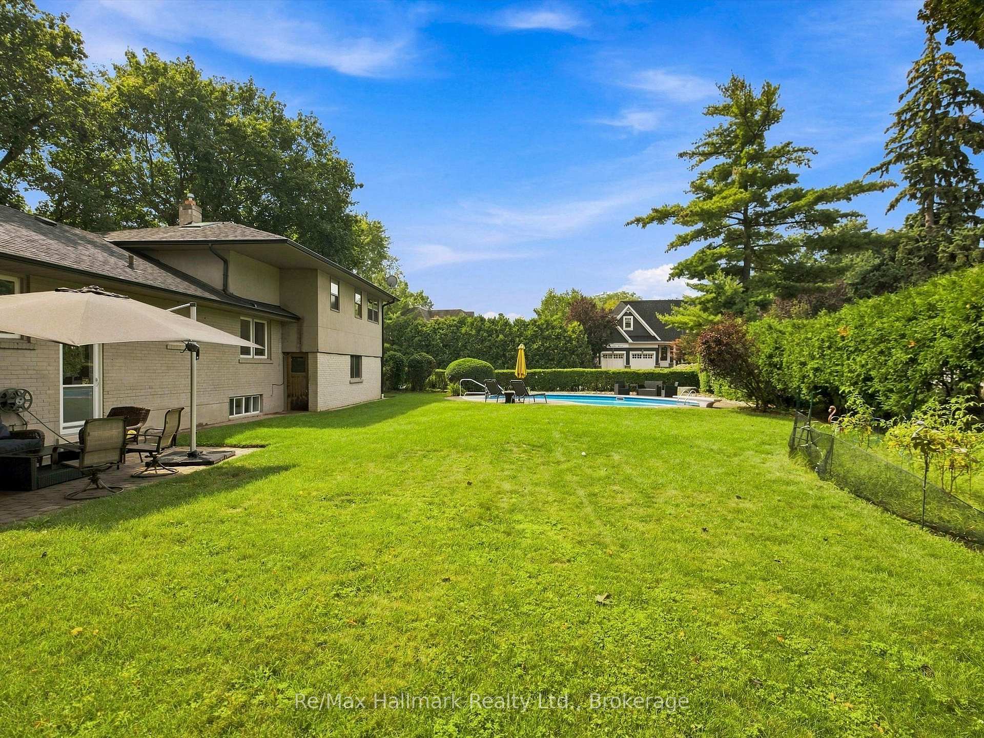 Backyard with a large lawn, swimming pool, and patio seating beside the house.