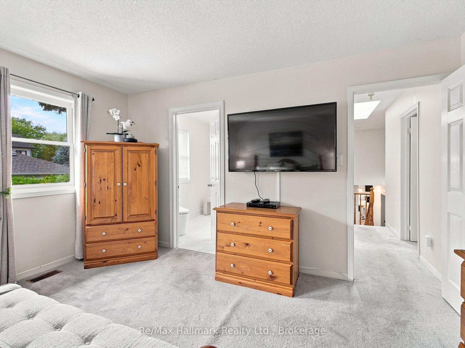 Furnished bedroom with a wall-mounted television, pine dressers, and a window overlooking trees.