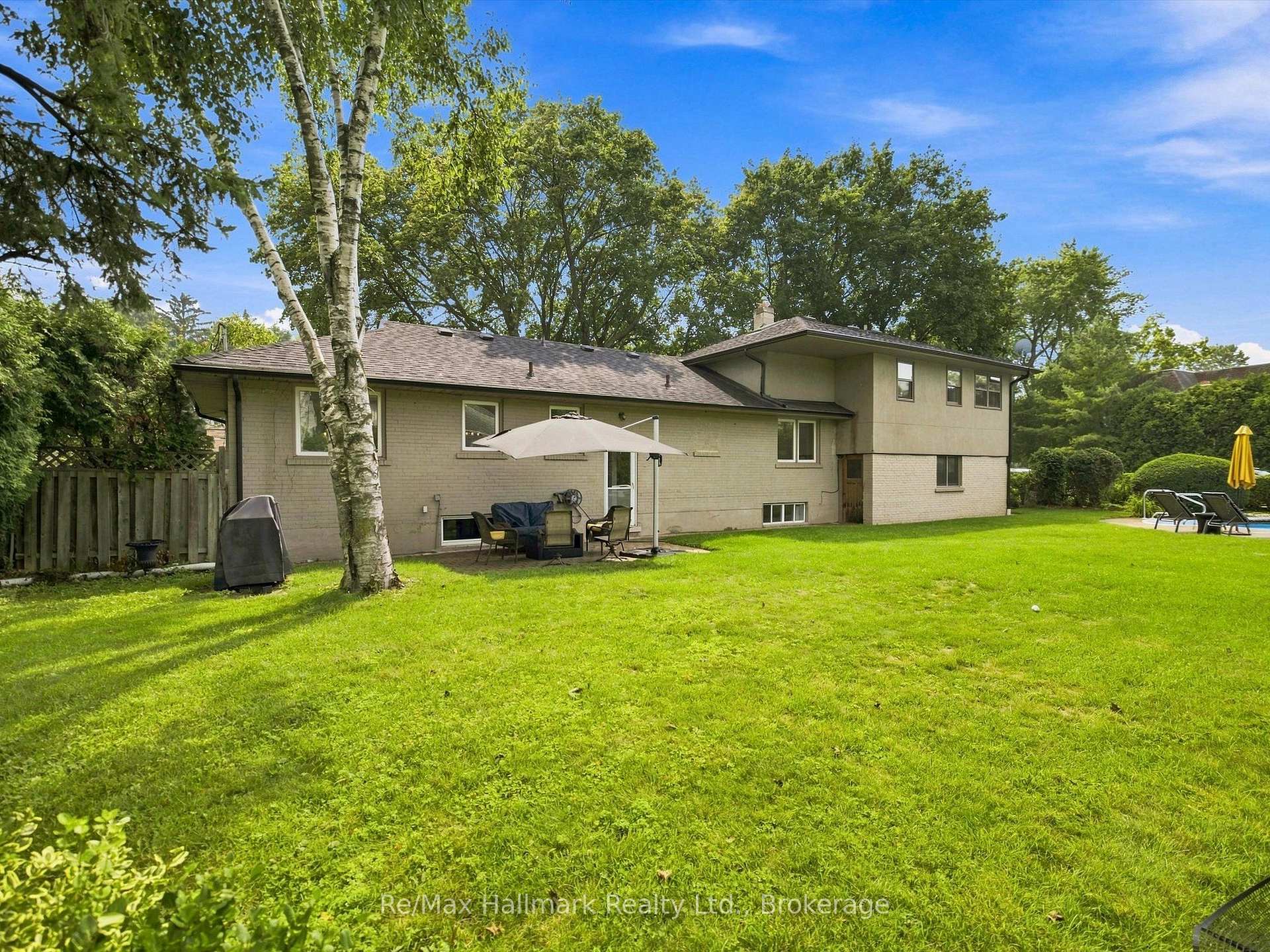 Rear of a two-storey brick house overlooking a broad lawn, with patio seating and a pool.