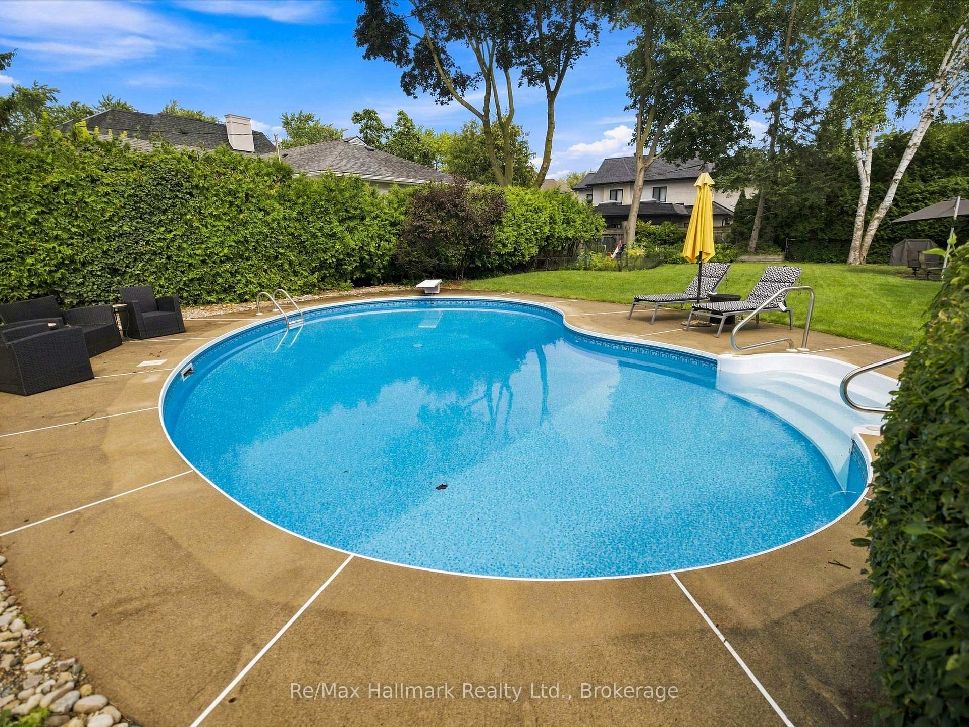 Backyard pool with curved blue basin, tan deck, lounge chairs, and yellow umbrella