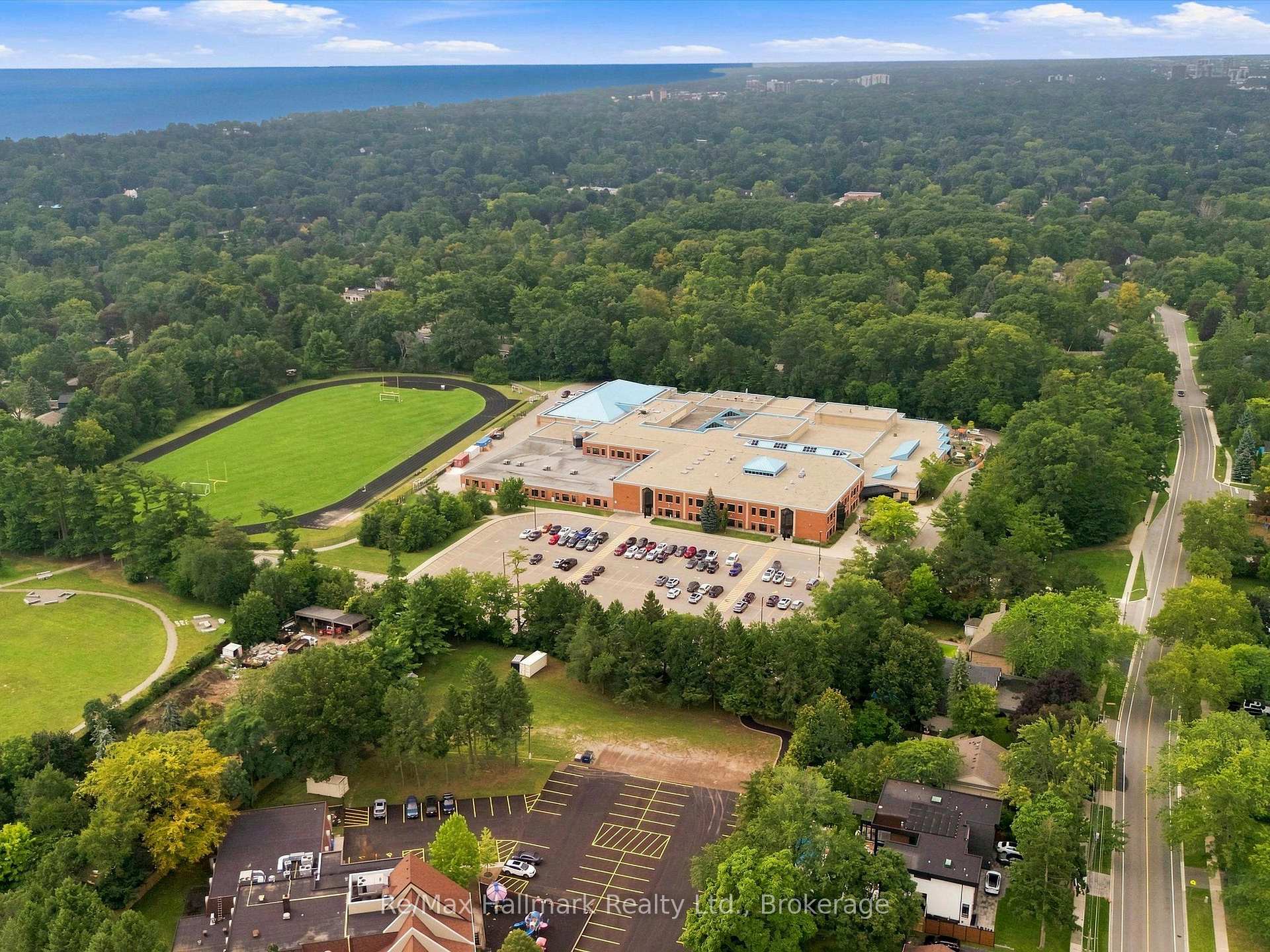 Aerial view of a brick building and running track surrounded by trees, with water on the horizon.