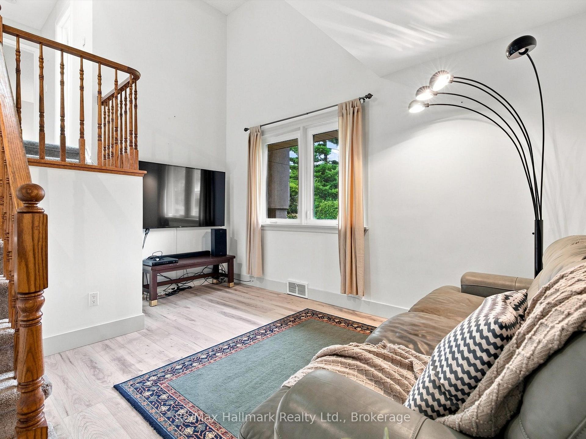 Living room with a wooden staircase, beige sofa, television, and patterned rug.