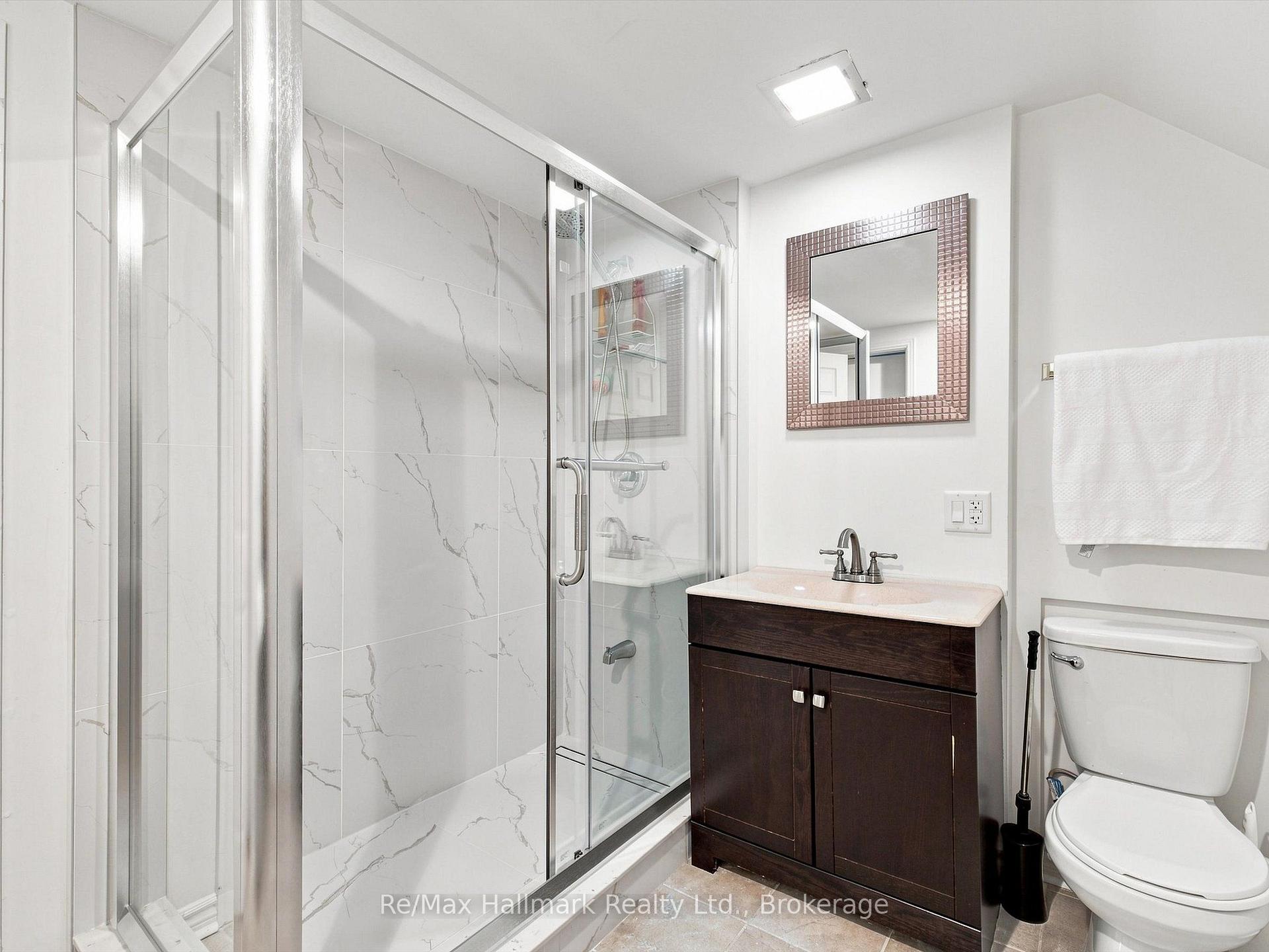 Bathroom with a glass shower, gray-veined tile, dark wood vanity, and toilet.