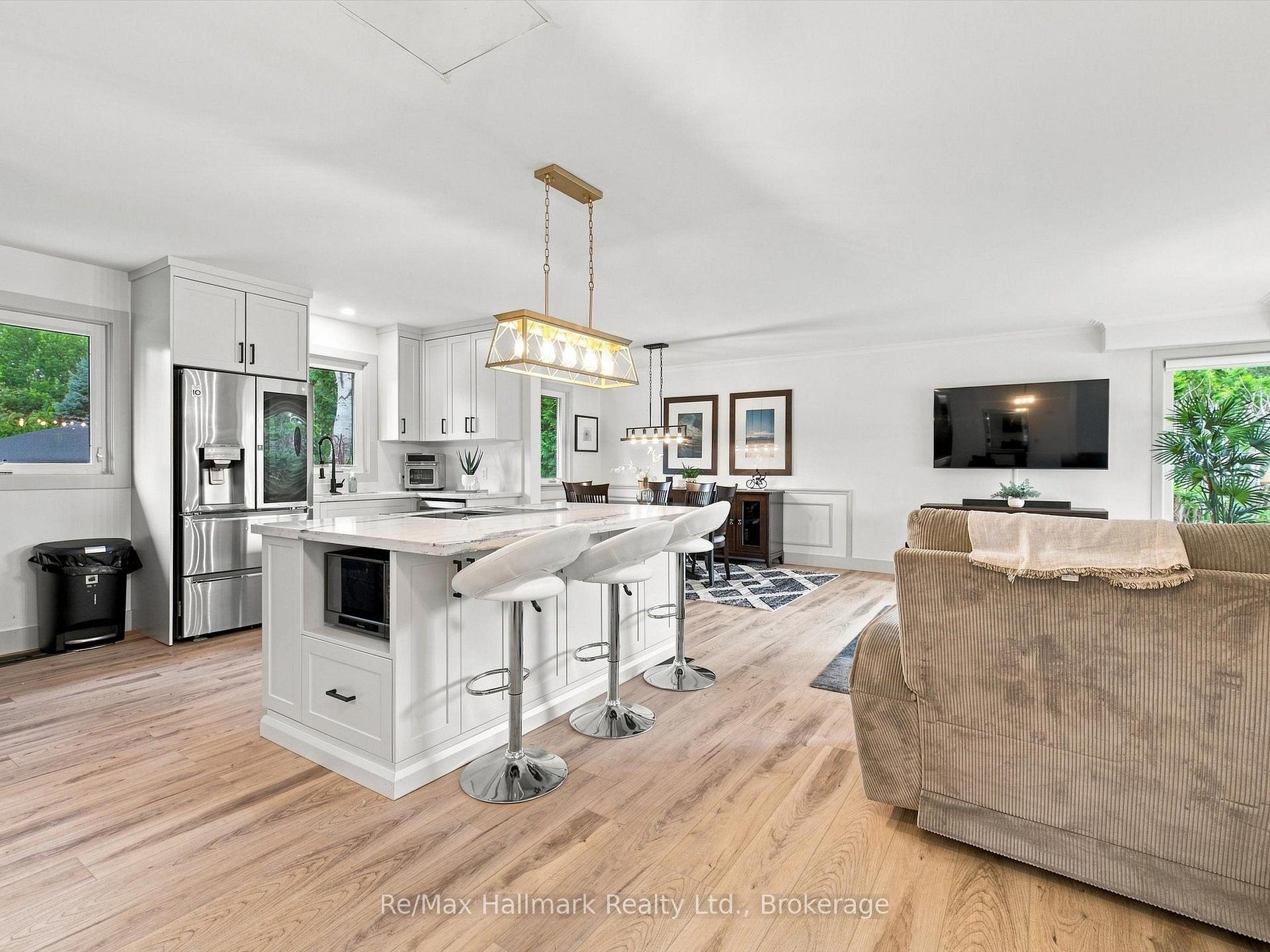 Open-plan kitchen with a large white island and bar stools beside a furnished living area.
