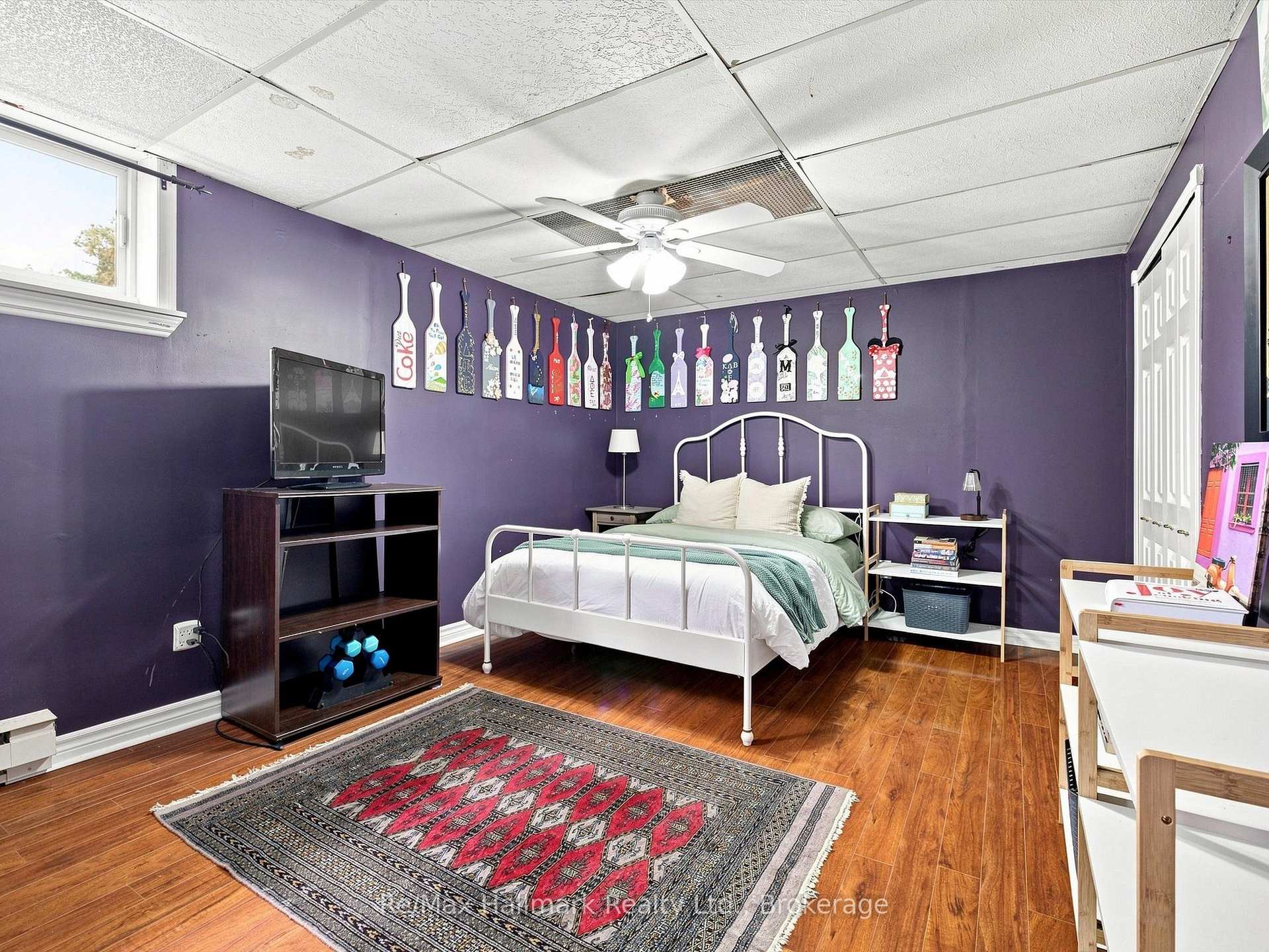 Bedroom with purple walls, a white metal bed, hardwood floors, and colorful paddle decorations.