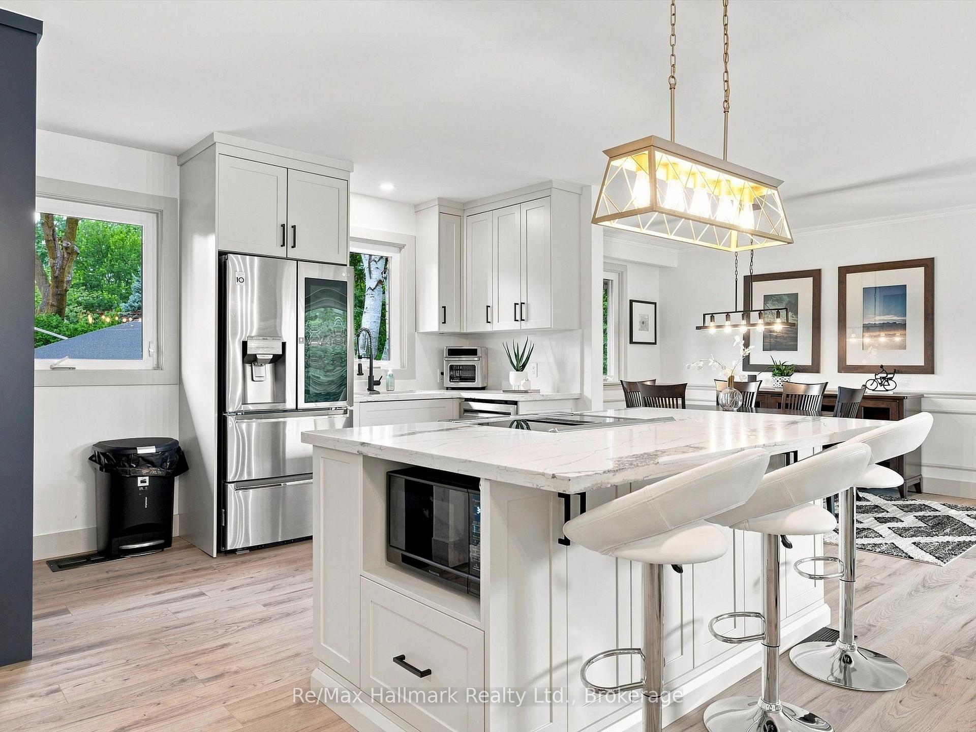 Bright white kitchen with a large island, bar stools, stainless steel refrigerator, and adjoining dining area.