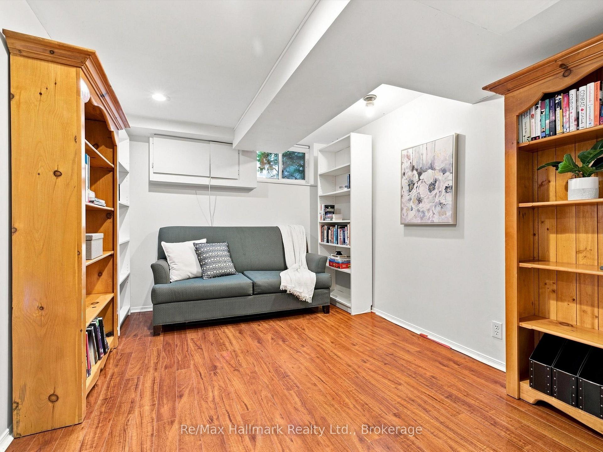 Basement sitting room with a gray sofa, built-in shelves, wooden bookcases, and warm wood flooring.