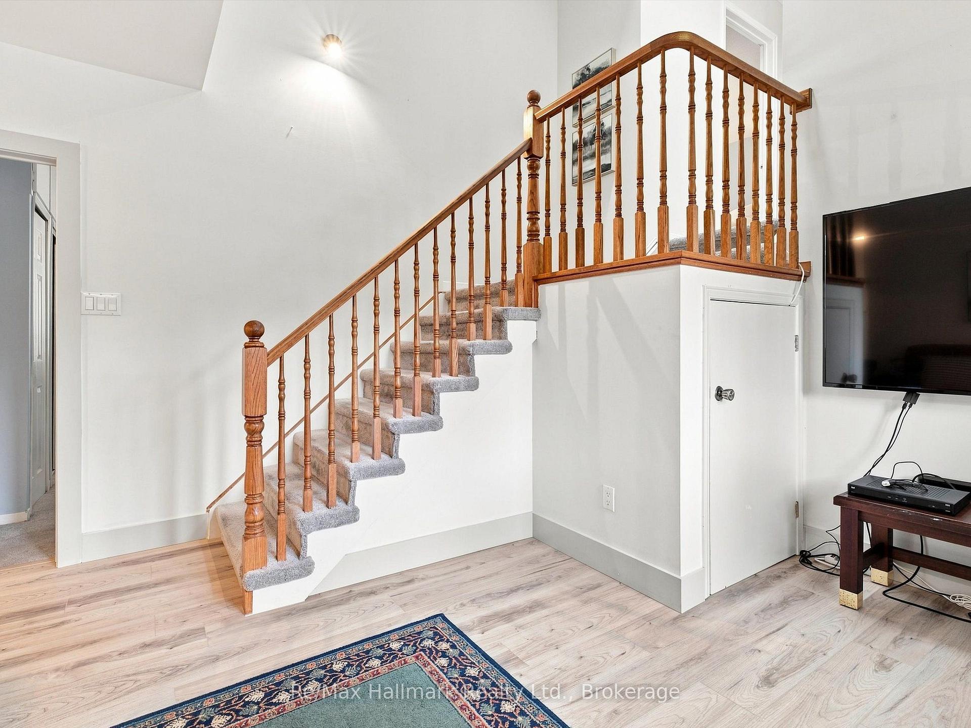 Carpeted staircase with a wooden railing and upper landing in a bright room.