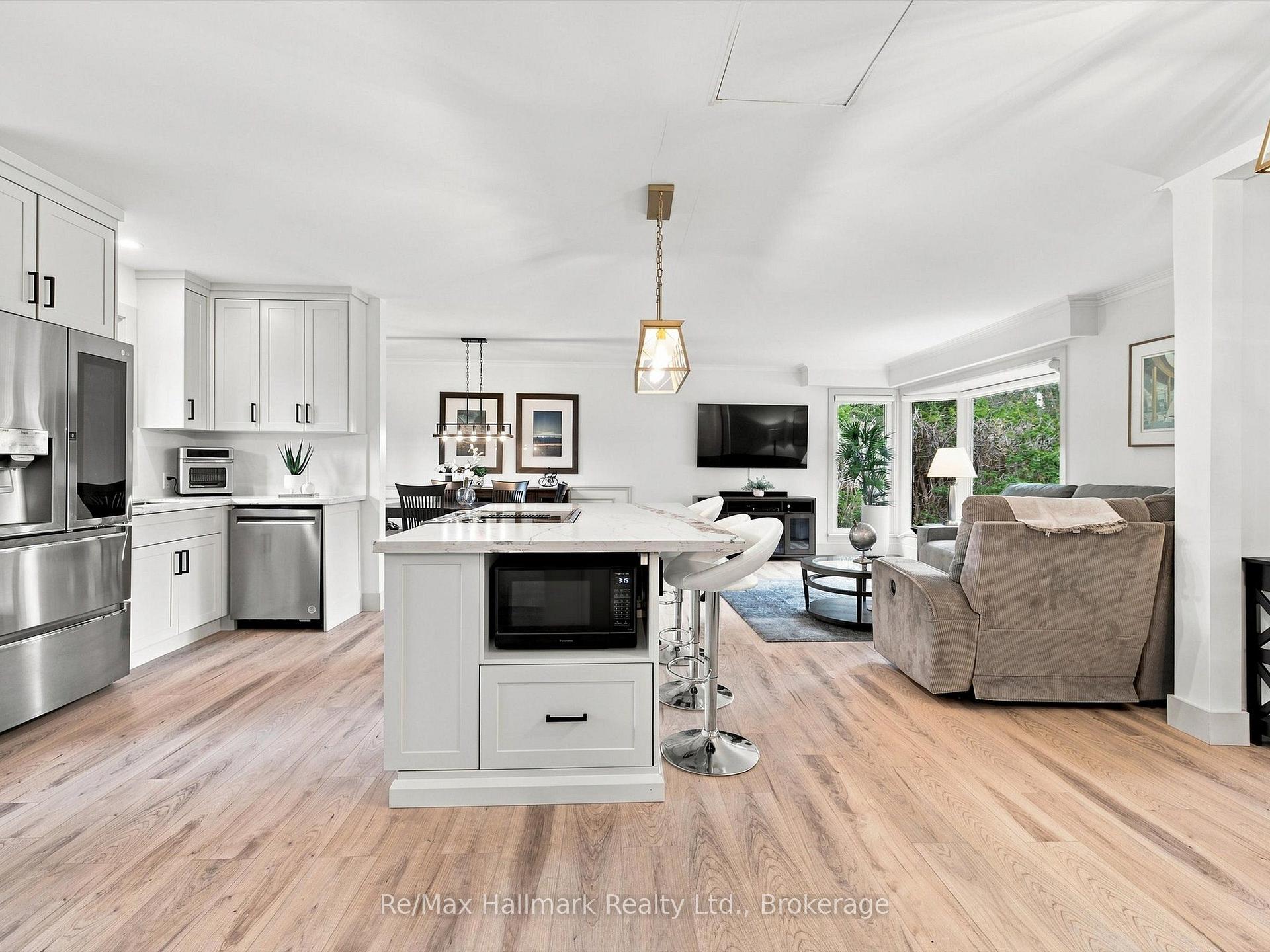 Open-plan kitchen and living room with a white island, stainless appliances, and light wood floors.