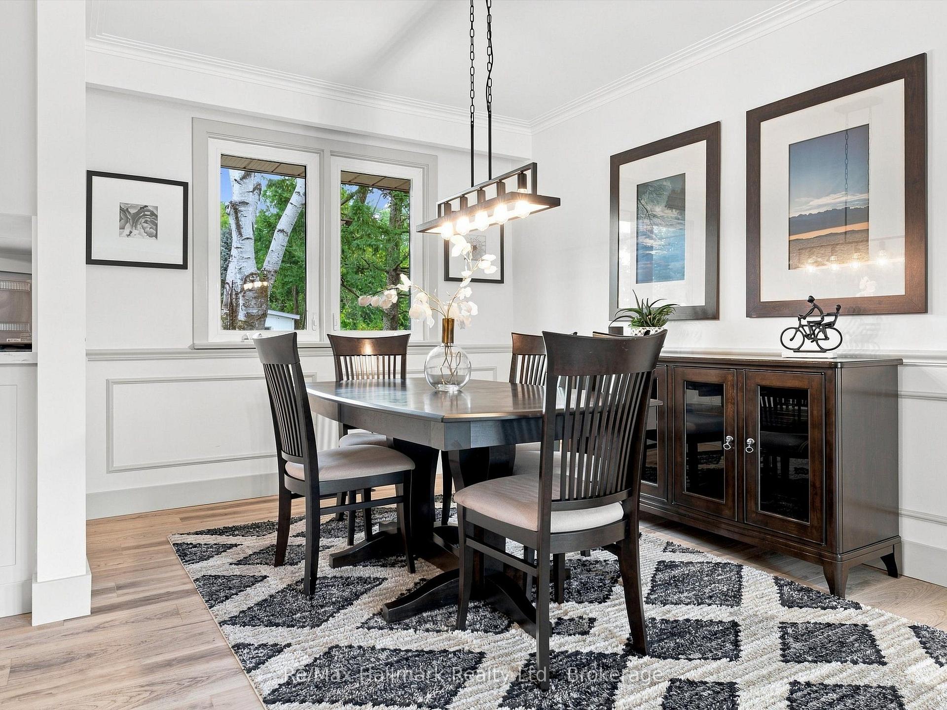 Dining room with a dark wood table, patterned rug, and large windows overlooking leafy trees.