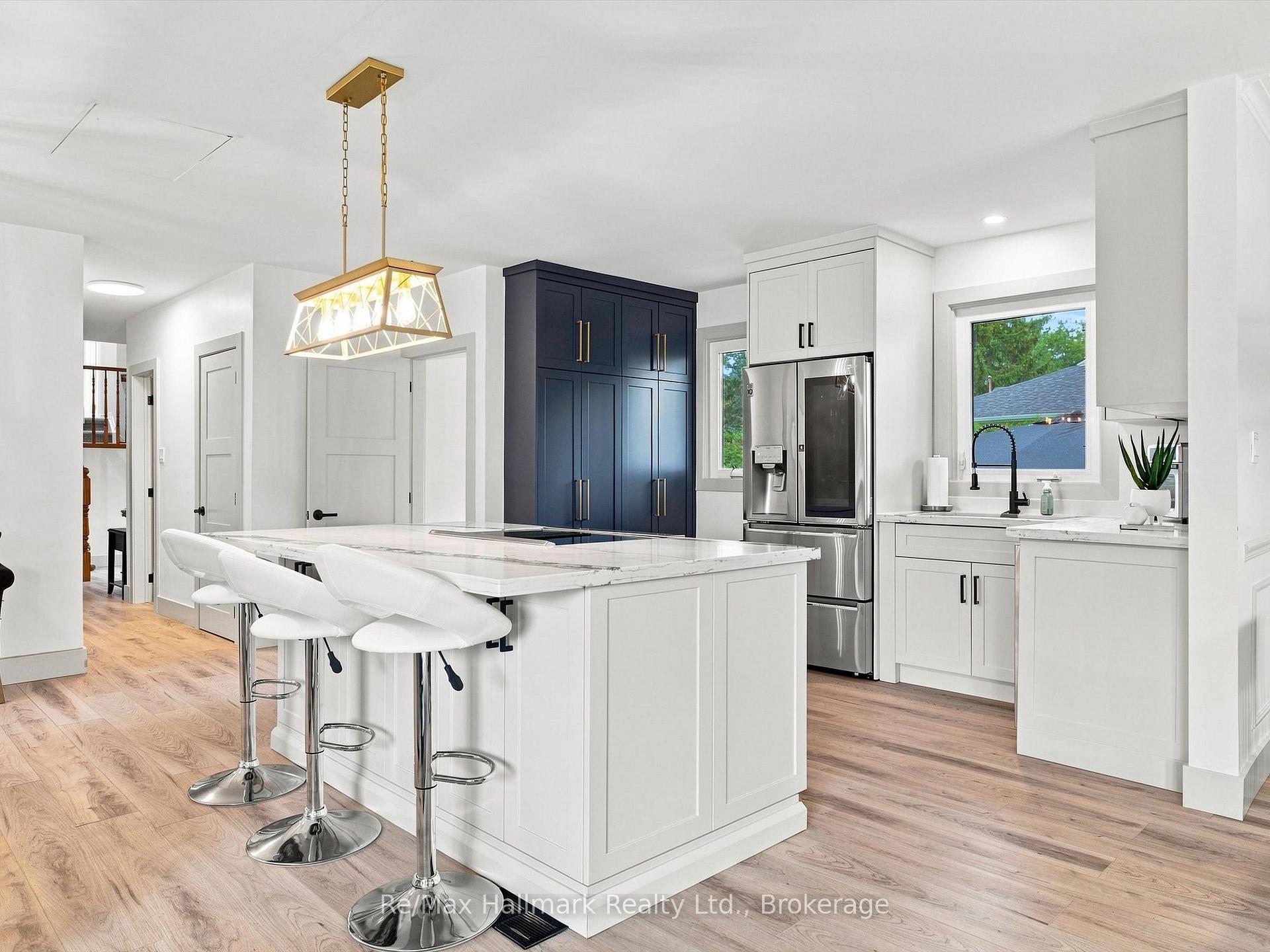 Modern kitchen with a marble-look island, navy cabinets, stainless steel refrigerator, and brass pendant light.