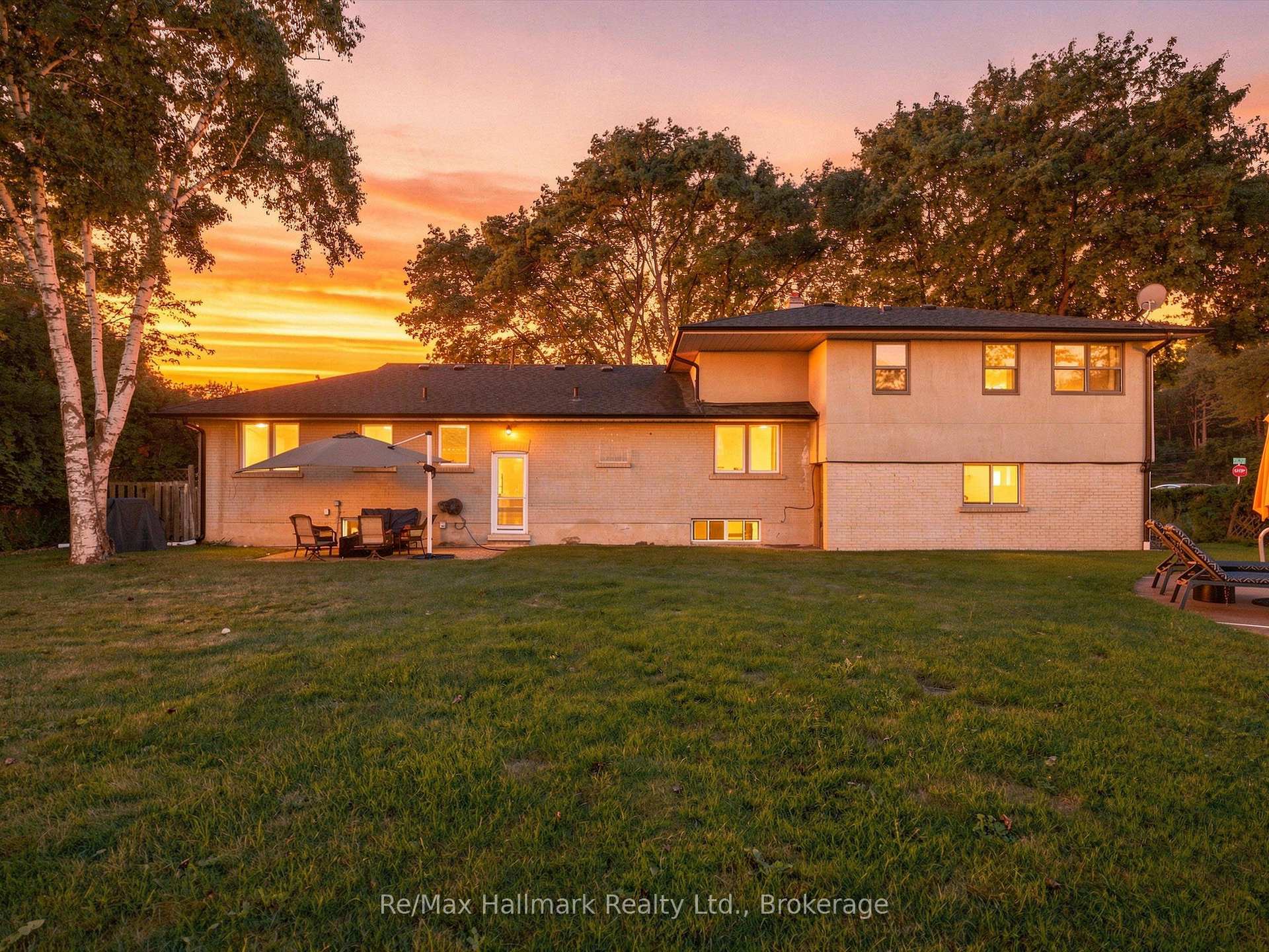 Two-story brick house and lawn at sunset, with patio seating and mature trees.